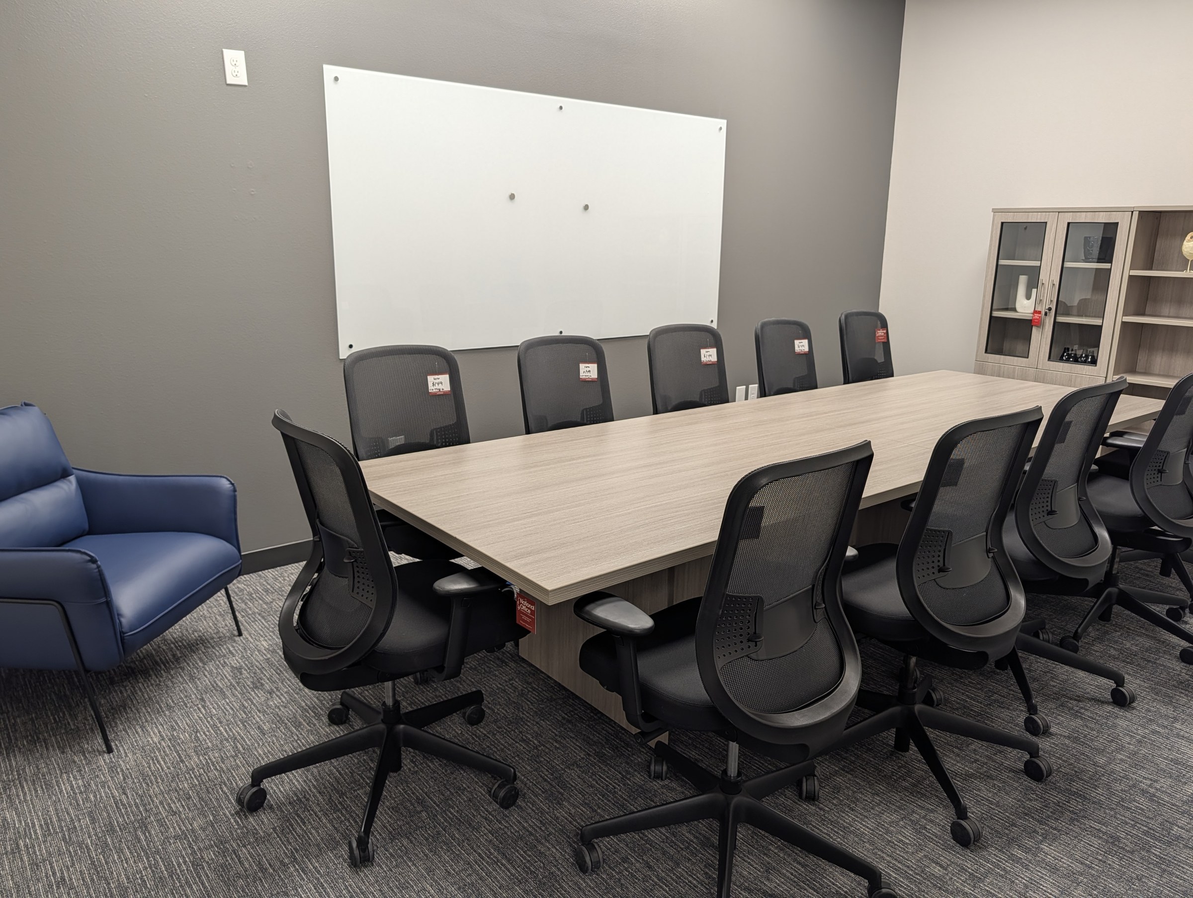 Conference room with a rectangular laminate table, black mesh conference chairs and a glass whiteboard