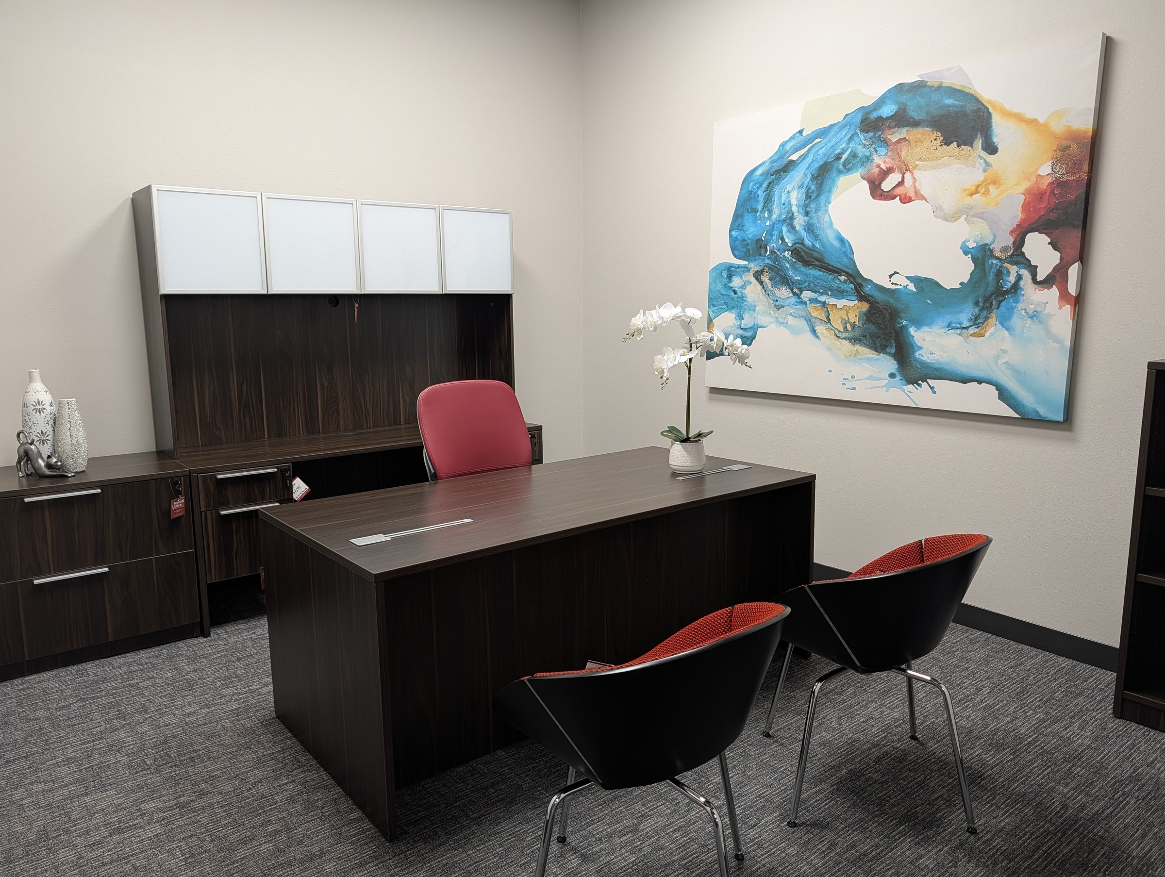 Private office with a dark laminate executive desk, overhead hutch storage and upholstered guest chairs