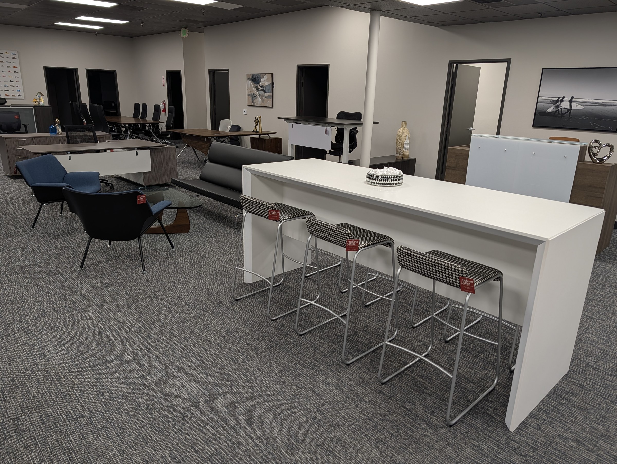 Irvine showroom floor with a standing-height meeting table, stools, lounge seating and desks on display