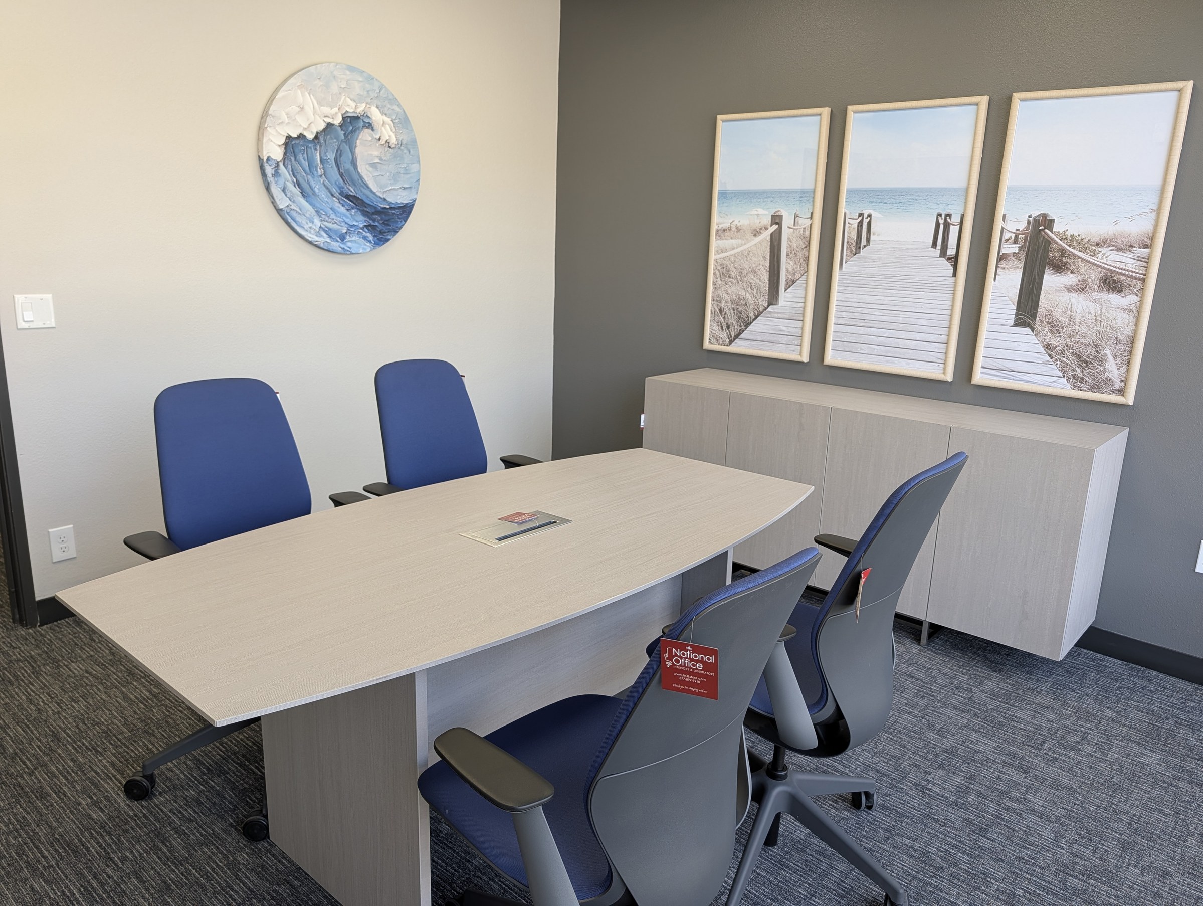 Small conference room with a boat shaped light laminate table, blue task chairs and a matching storage credenza